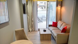 Ein modernes Wohnzimmer mit einer Couch, einem Couchtisch und einem Sessel. Ein großes Schiebeglastür führt zu einem Außenbereich mit Tisch und Stühlen.