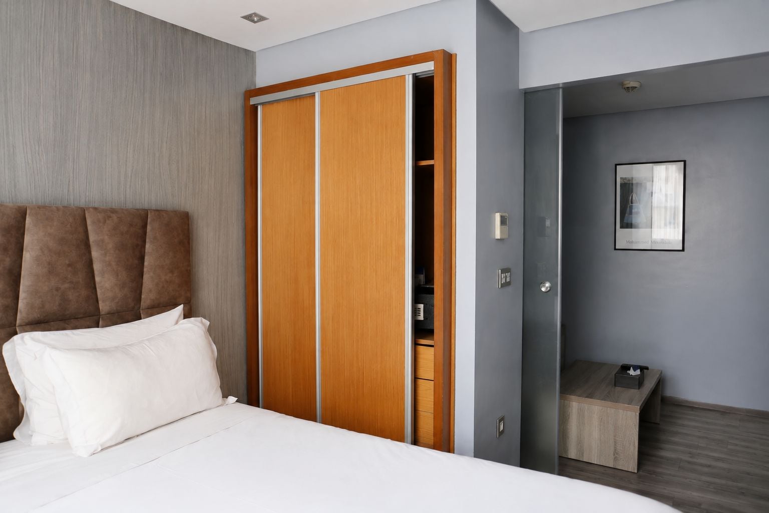 Une chambre d’hôtel moderne avec un grand lit, une armoire en bois, un petit bureau et un tableau encadré au mur.