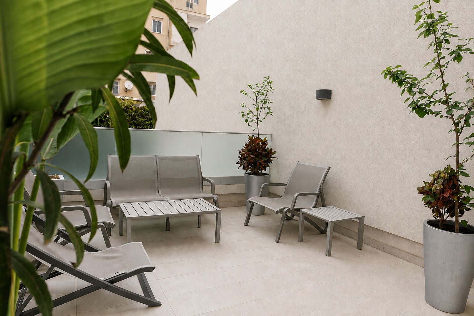 Een balkon met een zithoek, planten in potten en een wandlamp.
