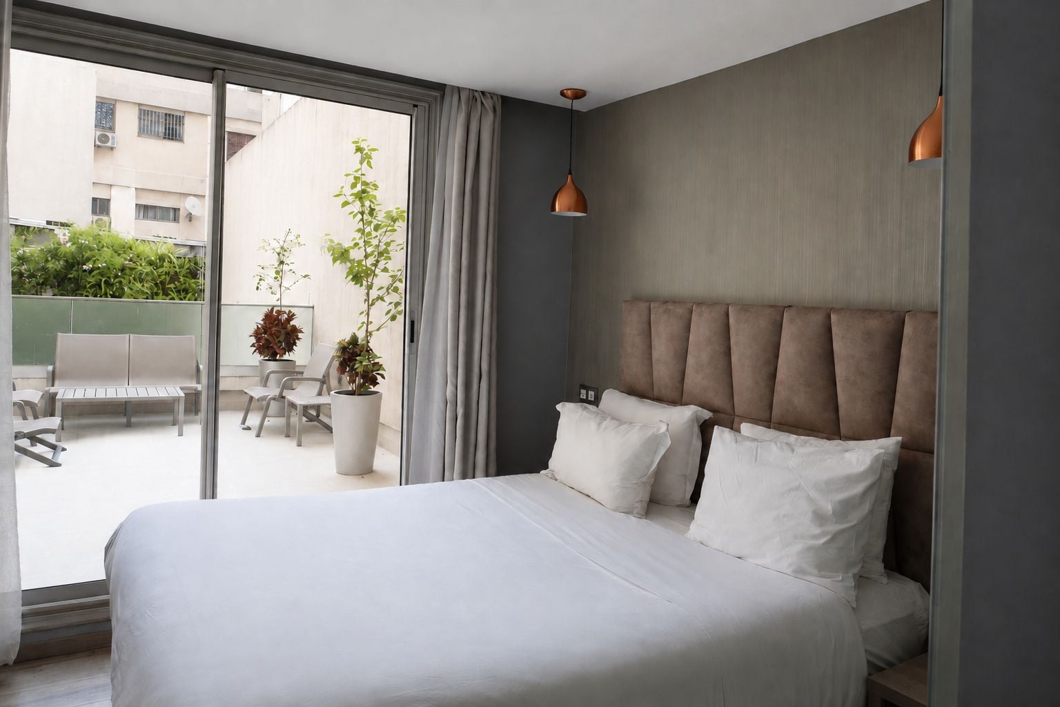Une chambre d’hôtel moderne avec un grand lit, une vue sur l’espace extérieur aménagé en salon et une grande fenêtre.