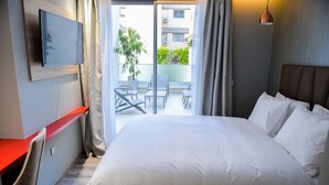 Ein Hotelzimmer mit Bett, Schreibtisch, Stuhl, Fernseher und einem Balkon mit Tisch und Stühlen.