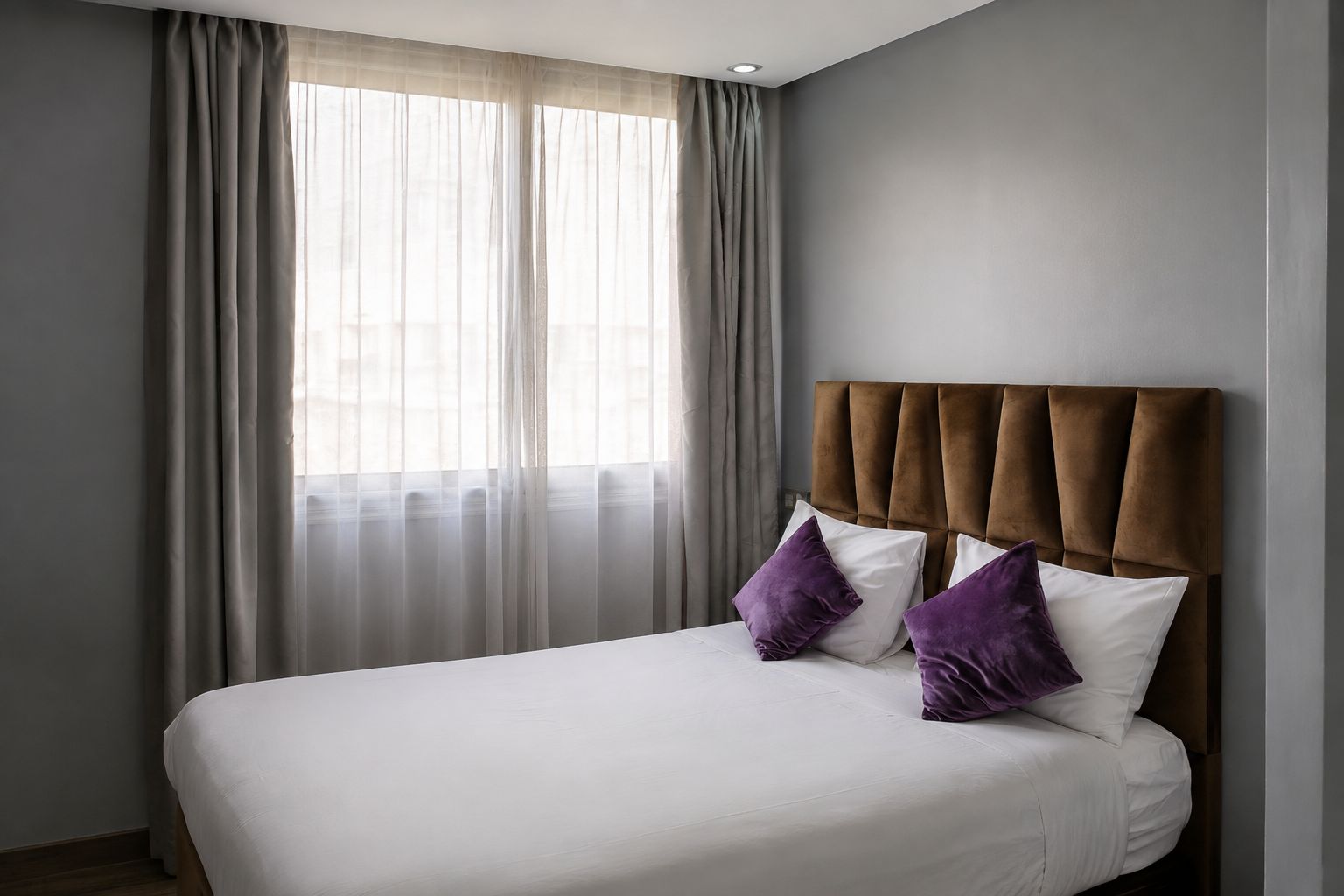 Habitación de hotel con cama, cabecero y ventana con cortinas.