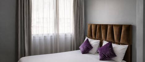 Habitación de hotel con cama, cabecero y ventana con cortinas.