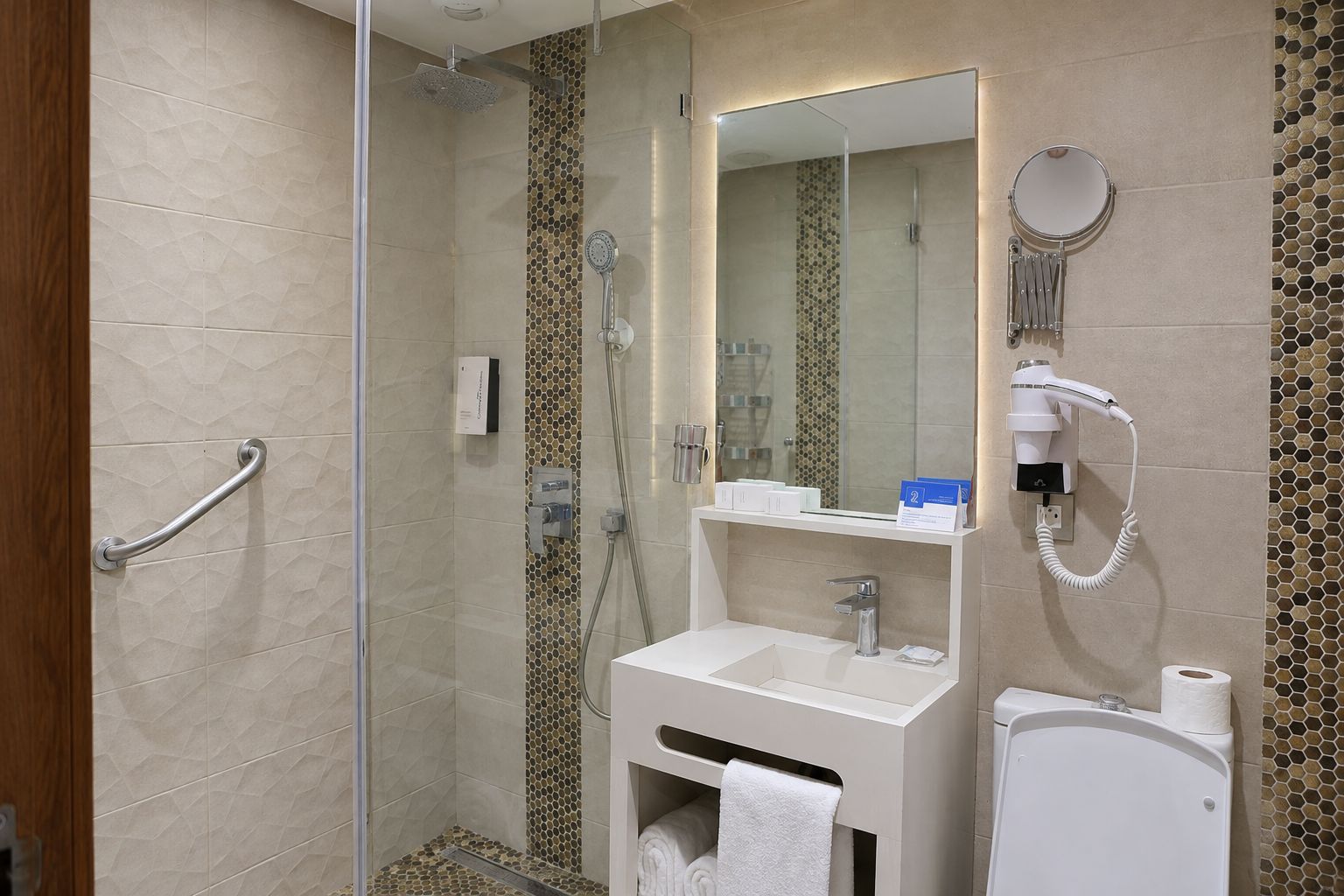 A modern bathroom with a glass shower enclosure, a white sink with a mirror, and a hairdryer on the wall.