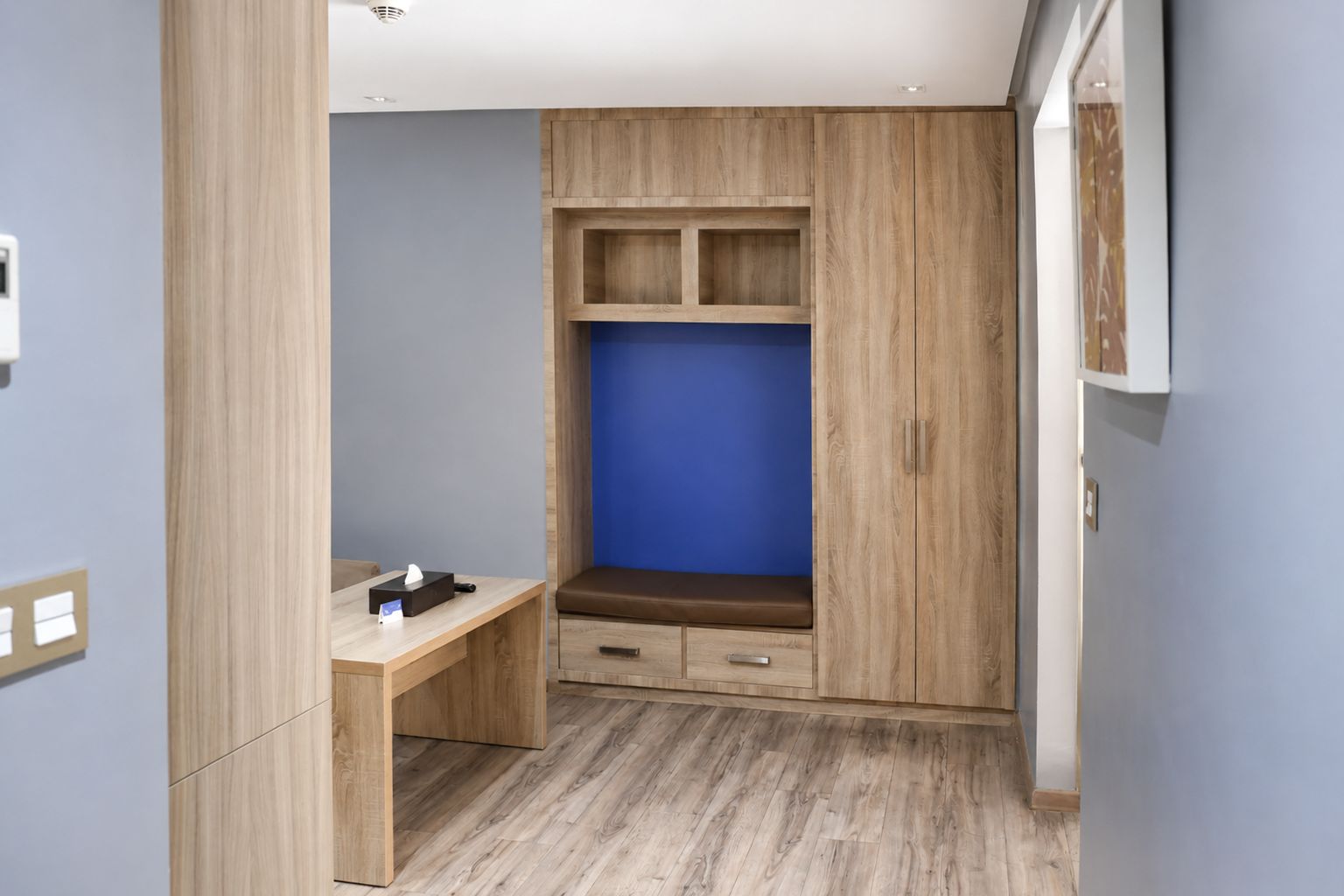 Une pièce comprenant une armoire en bois, un banc et un bureau avec une boîte de mouchoirs.
