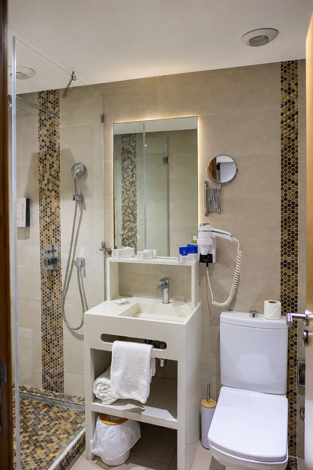 Un baño moderno con ducha envuelta en vidrio, lavamanos blanco, espejo y retrete.