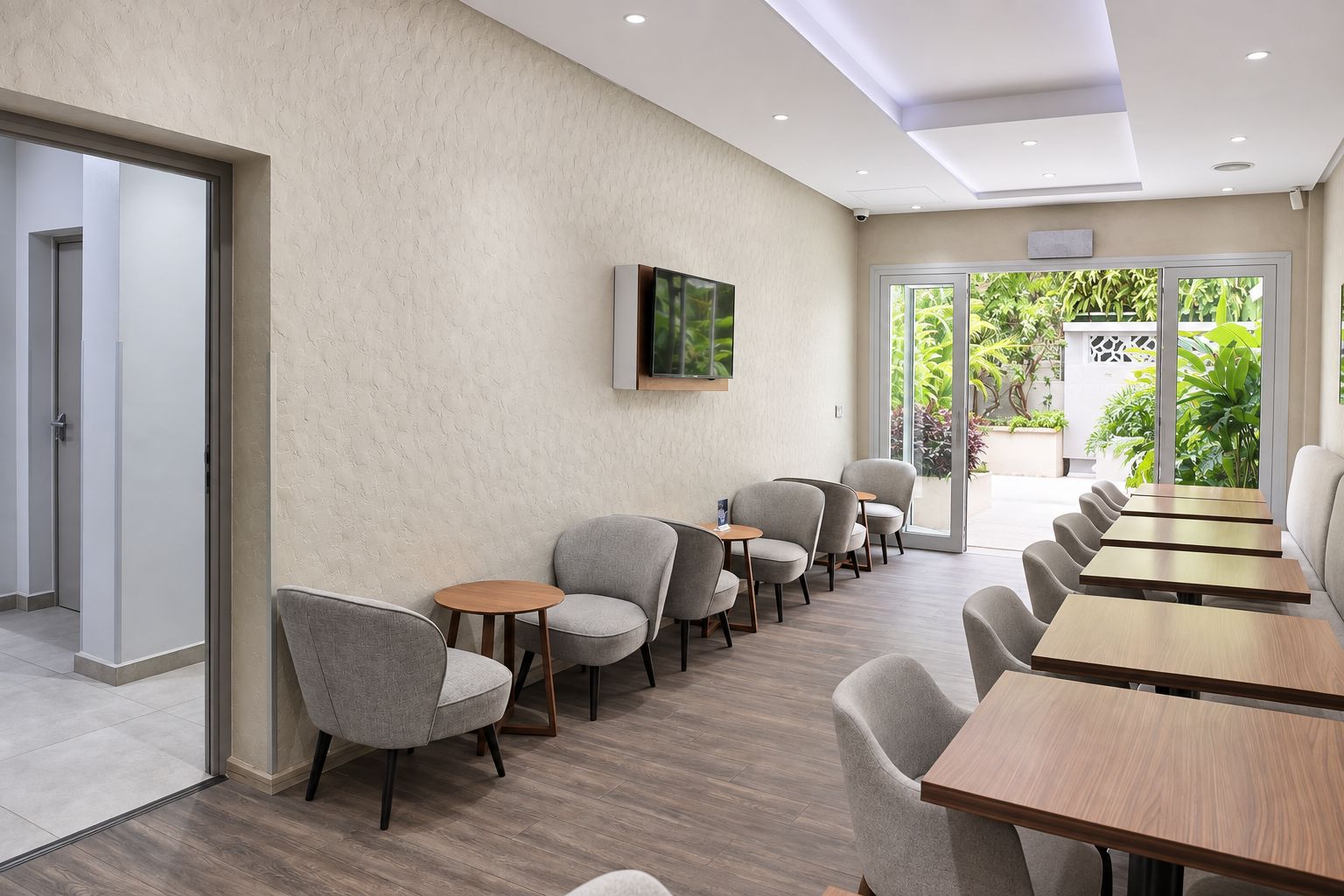 A conference room with a long table and chairs, a television mounted on the wall, and a view of greenery outside.