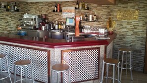 A bar area with a stone wall, bar counter, stools, and various bottles and glasses. - Hostal Ciudad de Lepe (Lepe)