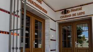 A building entrance with two doors labeled "Café Descuidados" and "Hostal Ciudad de Lepe". - Hostal Ciudad de Lepe (Lepe)