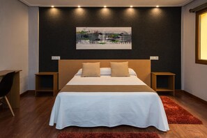 A modern bedroom with a large bed, two bedside tables, a desk, and a painting on the wall. - Hostal Ciudad de Lepe (Lepe)