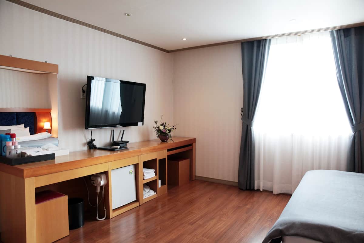 Ein Hotelzimmer mit einem Holzbüro, einem Flachbildfernseher, einem Bett und einem Fenster mit Vorhängen.