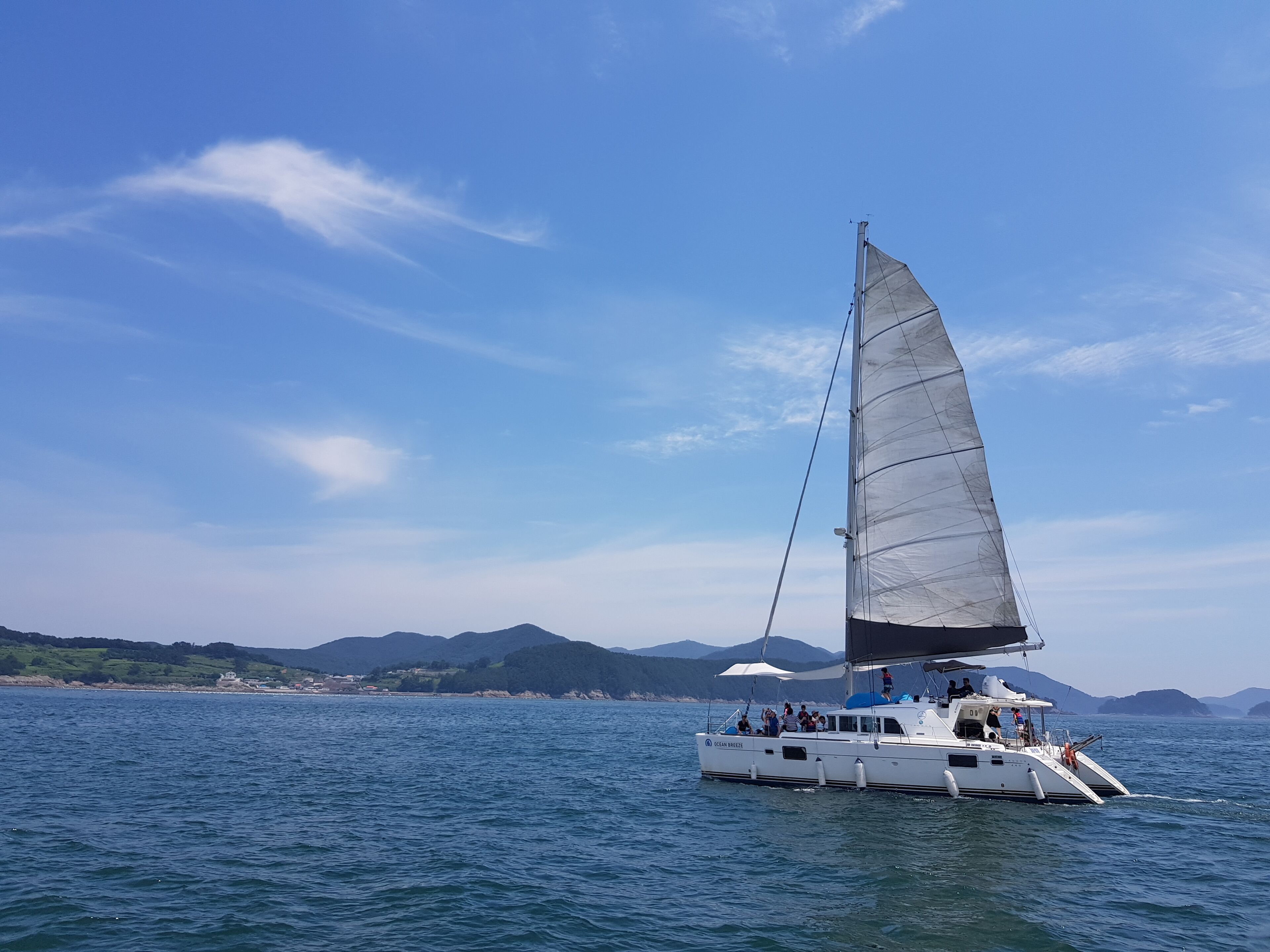 Ein Segelboot mit Passagieren auf ruhiger See, umgeben von Bergen und wolkenlosem Himmel.
