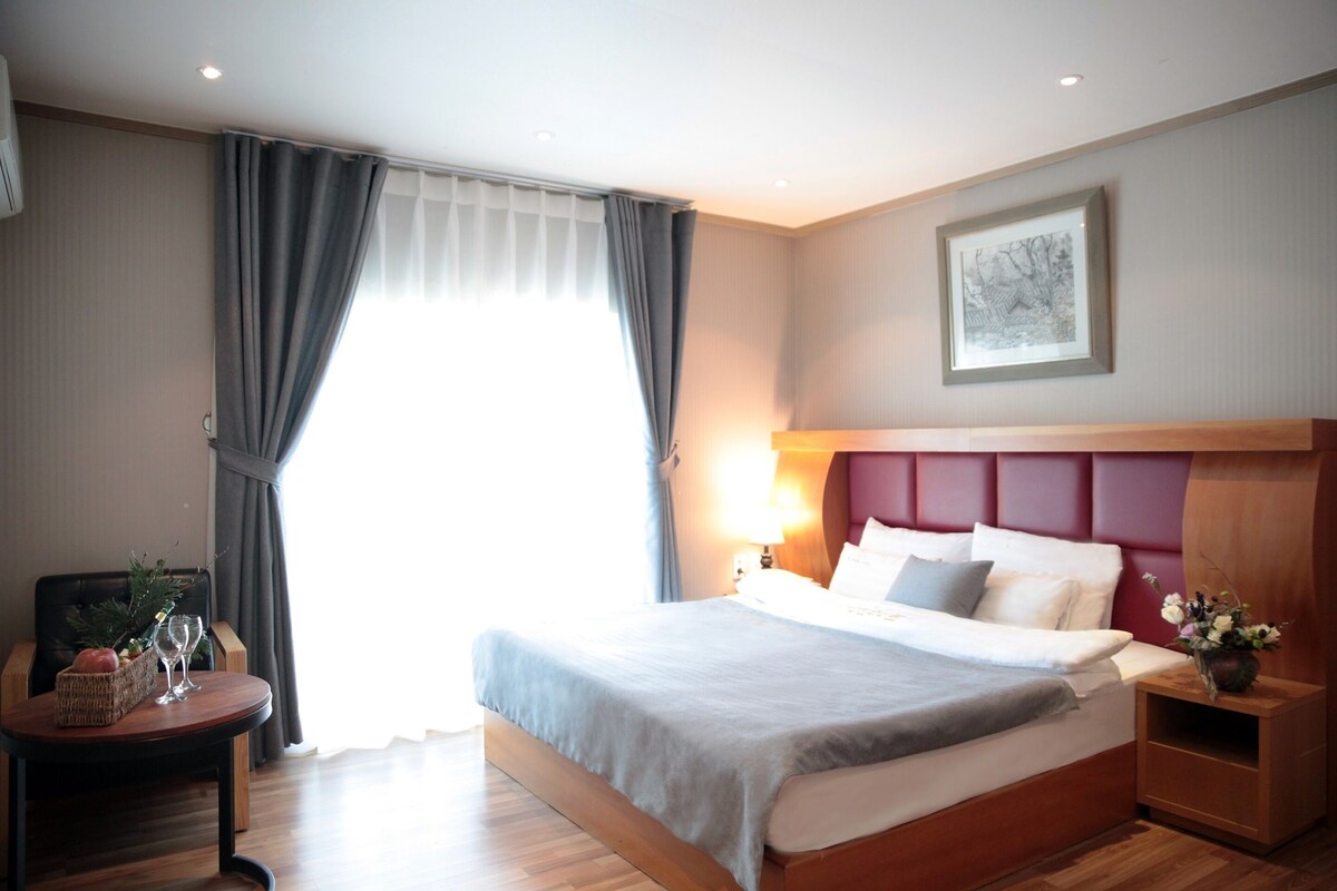 Een hotelkamer met een bed, nachtkastje, lamp en een lijst aan de muur.