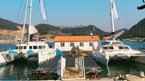 A marina with several sailboats docked, a small building with a red roof, and hills in the background. - La Belle Hotel In Tongyeong (Tongyeong)