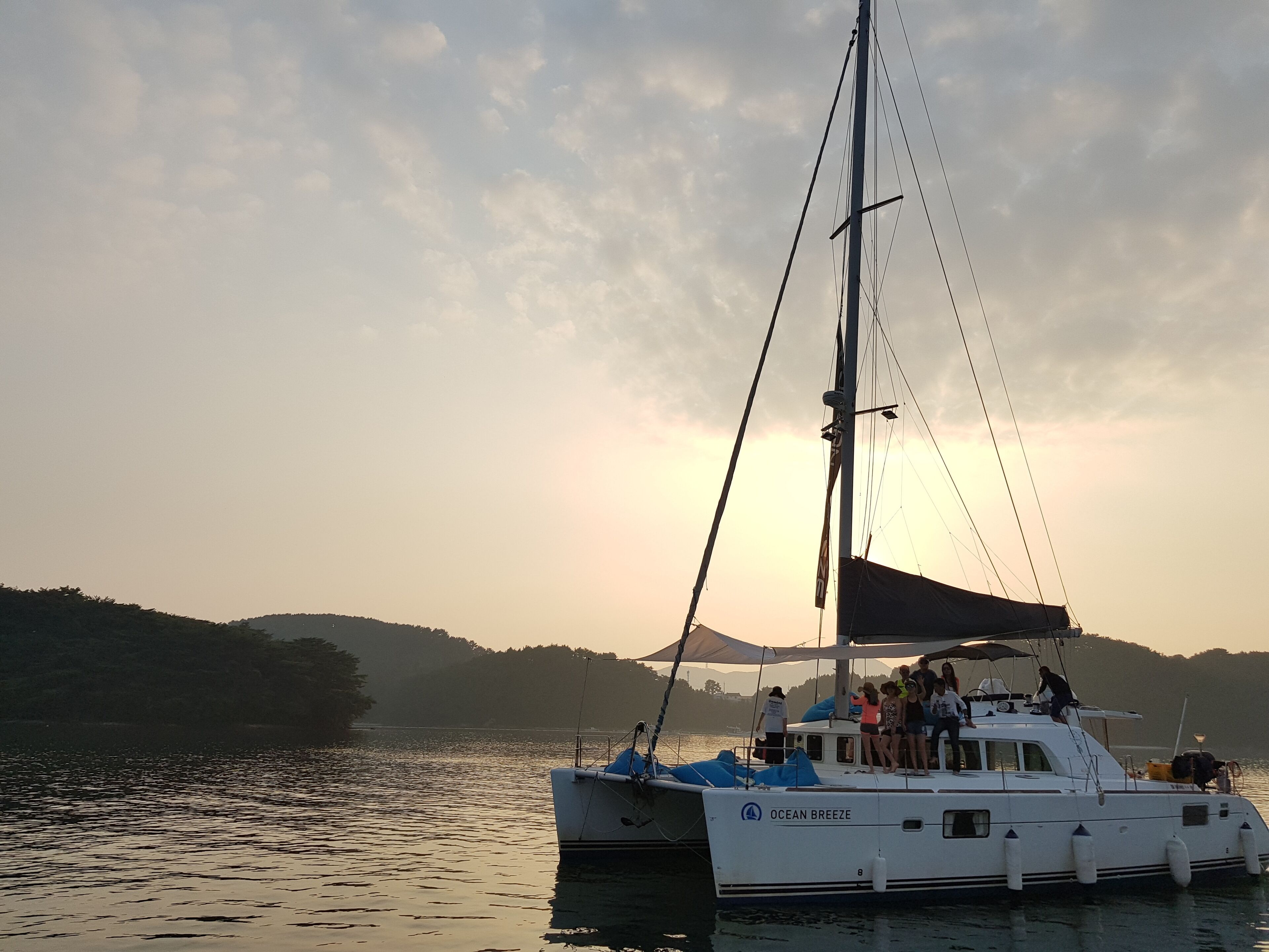 A sailboat named "Ocean Breeze" docked at a harbor with a mountainous backdrop.