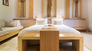 A bedroom with a large bed, a wooden bench, and three wooden frames on the wall. - Royal Beach Hôtel (Nosy Be)