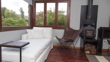 Un dormitorio con cama, una silla, una mesa, chimenea y ventana con vistas a árboles.