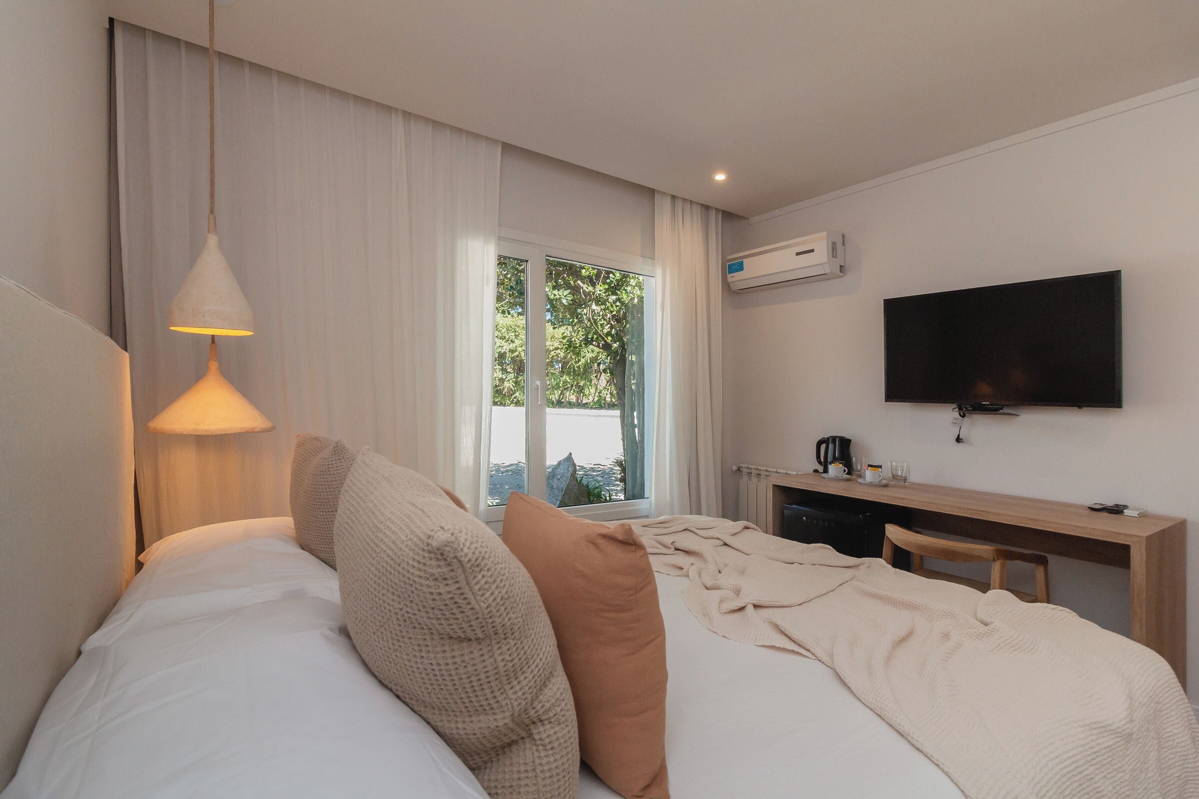 A hotel room with a bed, a desk, a television, and a window with curtains.