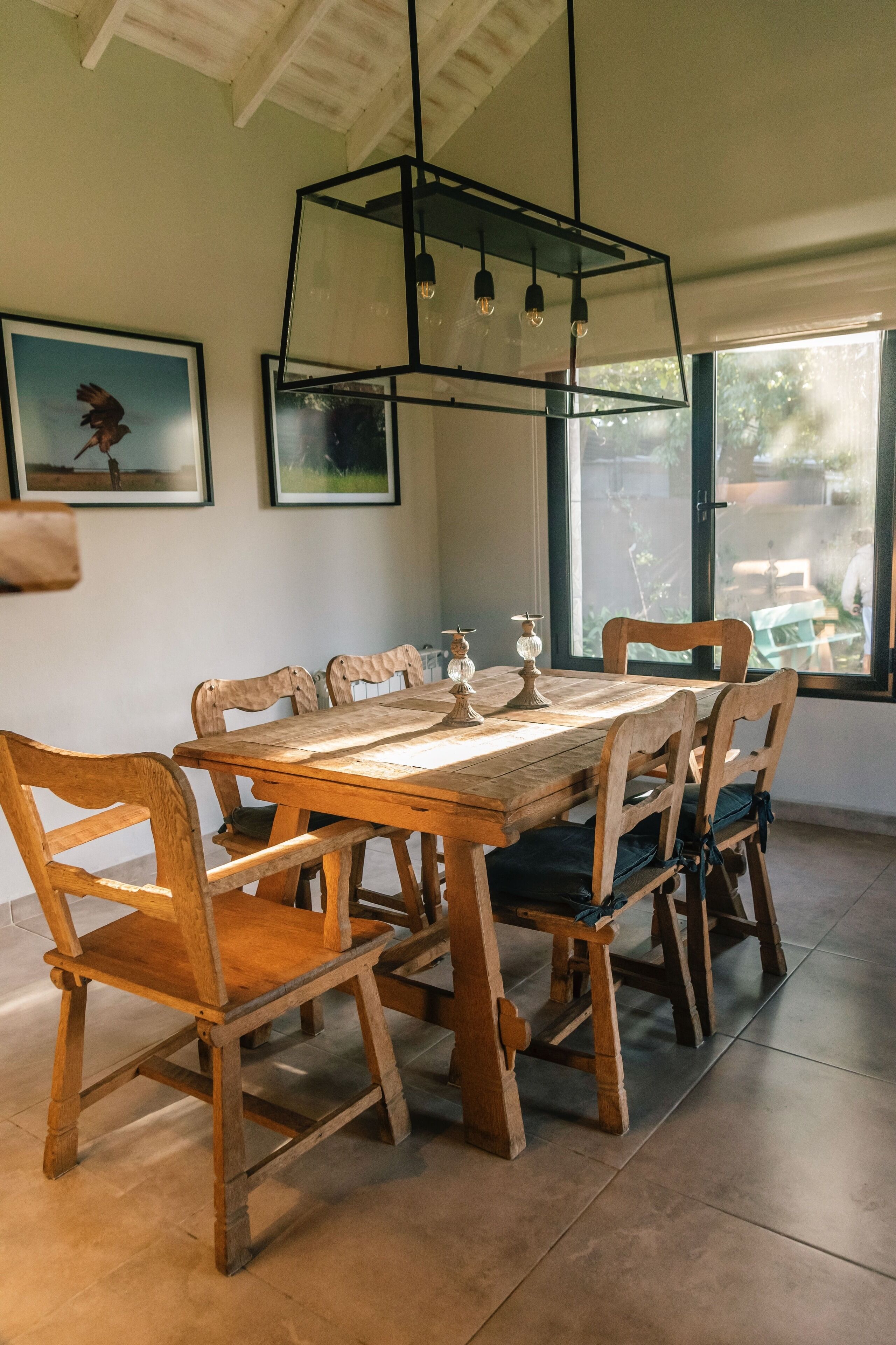 Un comedor con una mesa y sillas de madera, una lámpara colgante y cuadros en la pared.
