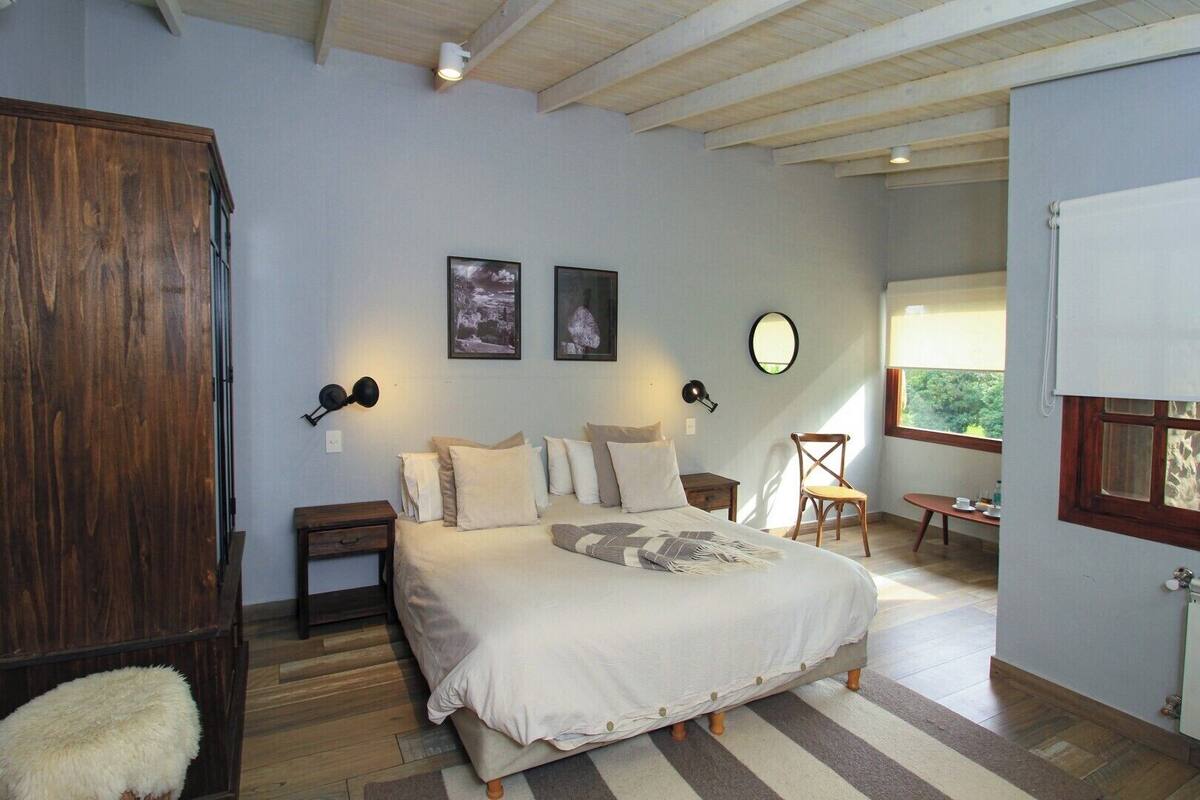Une chambre avec un grand lit, deux lampes fixées au mur, une armoire en bois et une petite table avec une chaise.