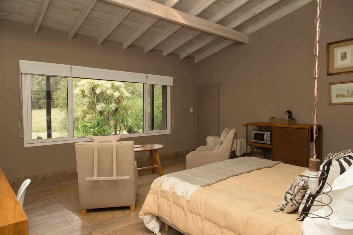 Une chambre avec un grand lit, un bureau, une chaise et une fenêtre donnant sur un paysage verdoyant.