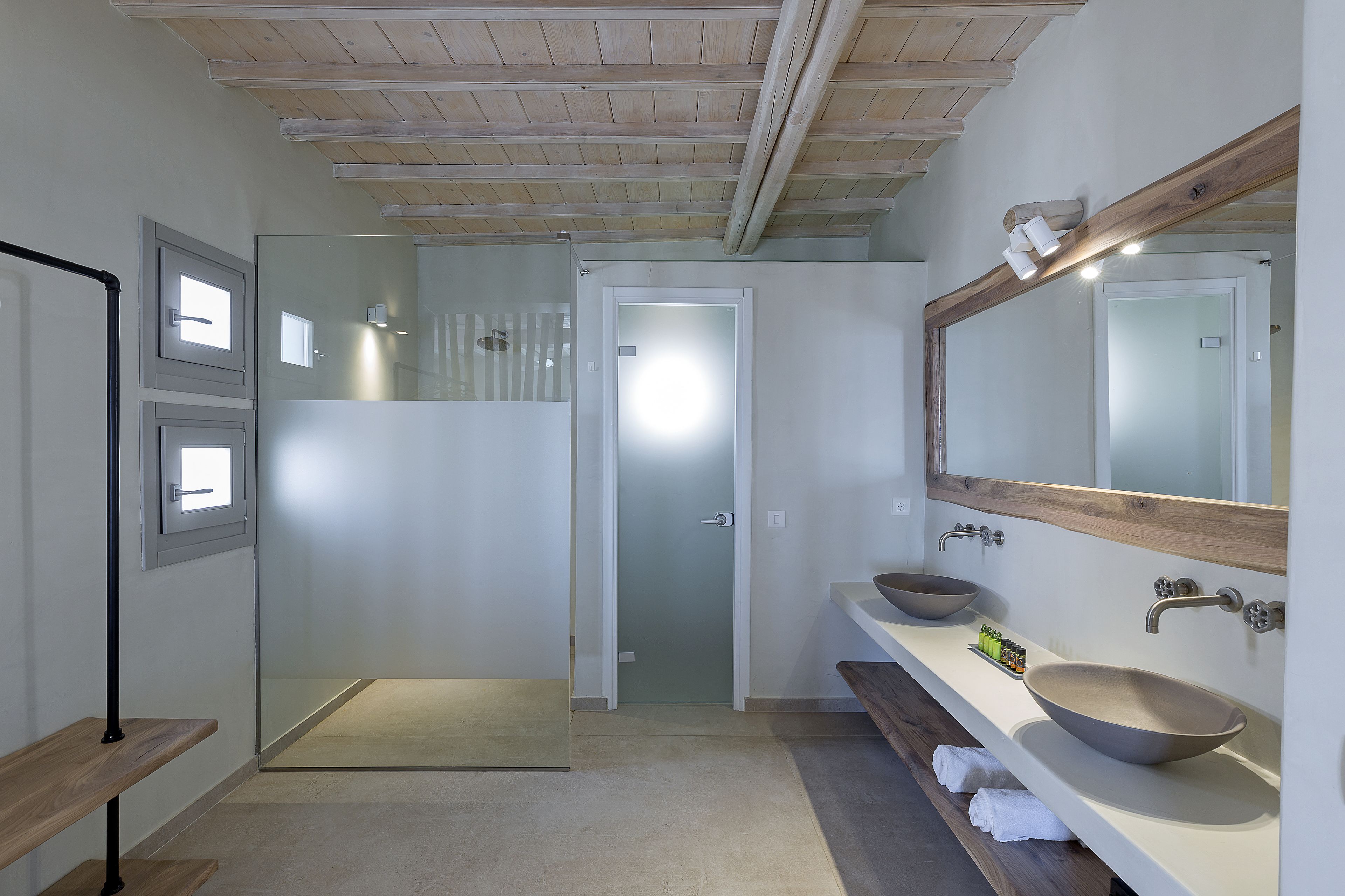 A modern bathroom with a large mirror, two sinks, and a shower area.