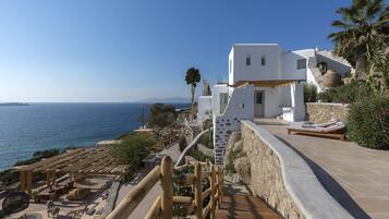 Una propiedad costera con un muro de piedra, terraza de madera y zona de estar al aire libre con vistas al mar.