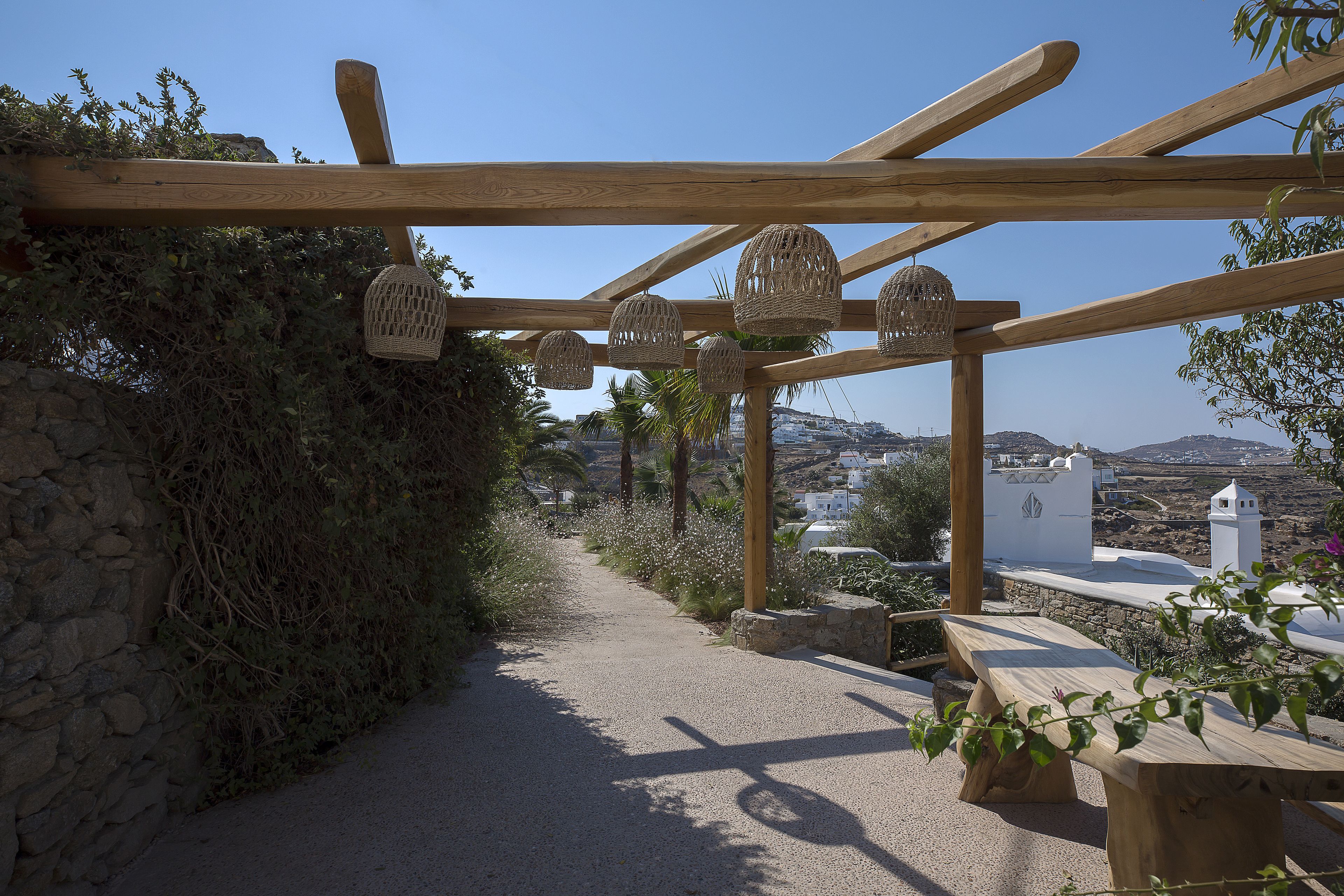 A wooden pergola with woven baskets hanging from the beams, a gravel path, and a bench.