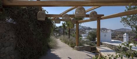 A wooden pergola with woven baskets hanging from the beams, a gravel path, and a bench.