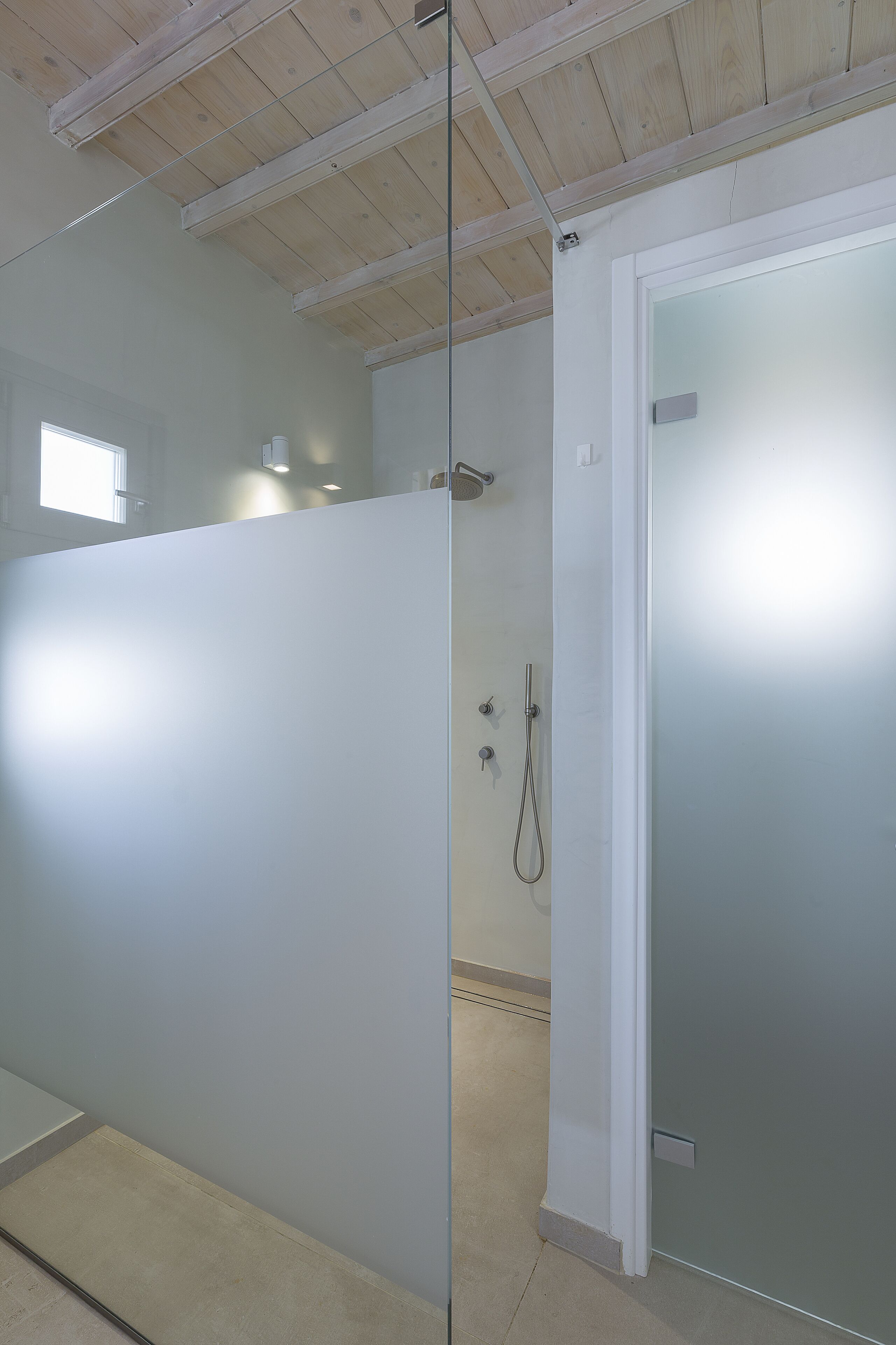 A modern bathroom with a glass partition, a shower, and a frosted door.