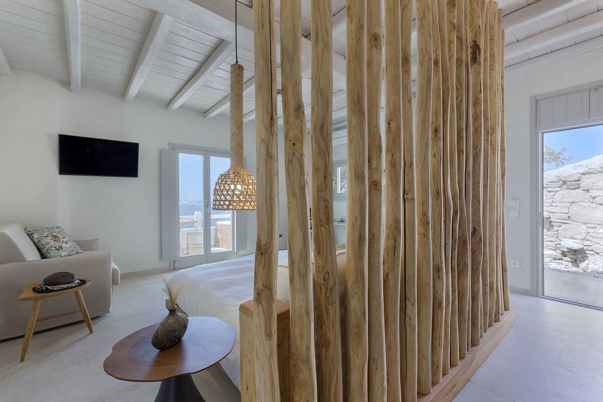 Uma sala de estar moderna com um sofá, uma mesa de madeira pequena, um vaso decorativo e um divisório de madeira.