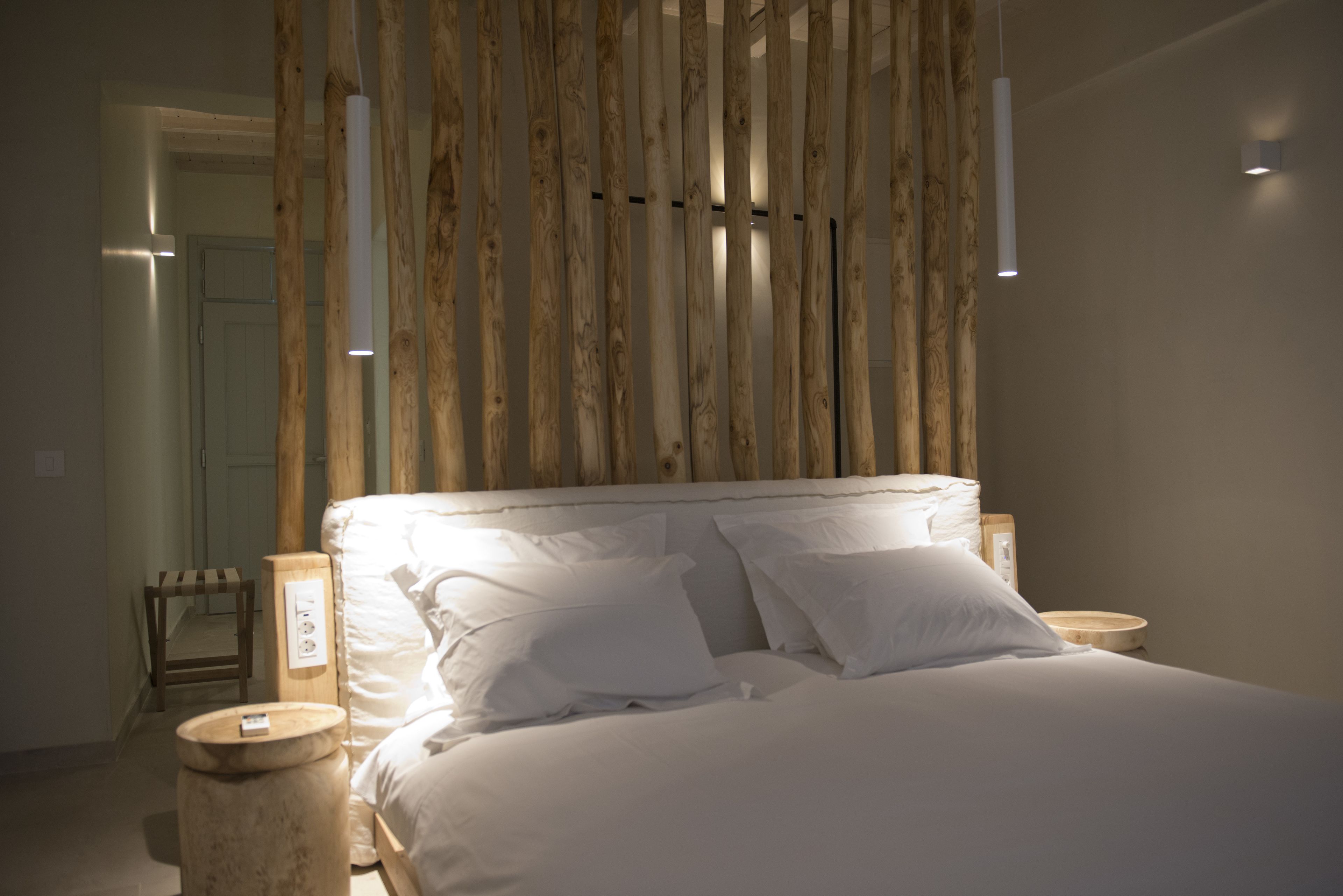 Cama bem arrumada com lençóis e almofadas brancos, cabeceira de madeira e mesas de cabeceira com abajures.