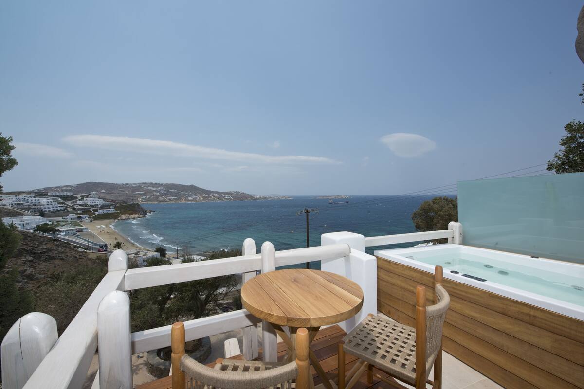Varanda com mesa e cadeiras de madeira, com vista para uma praia e o mar.