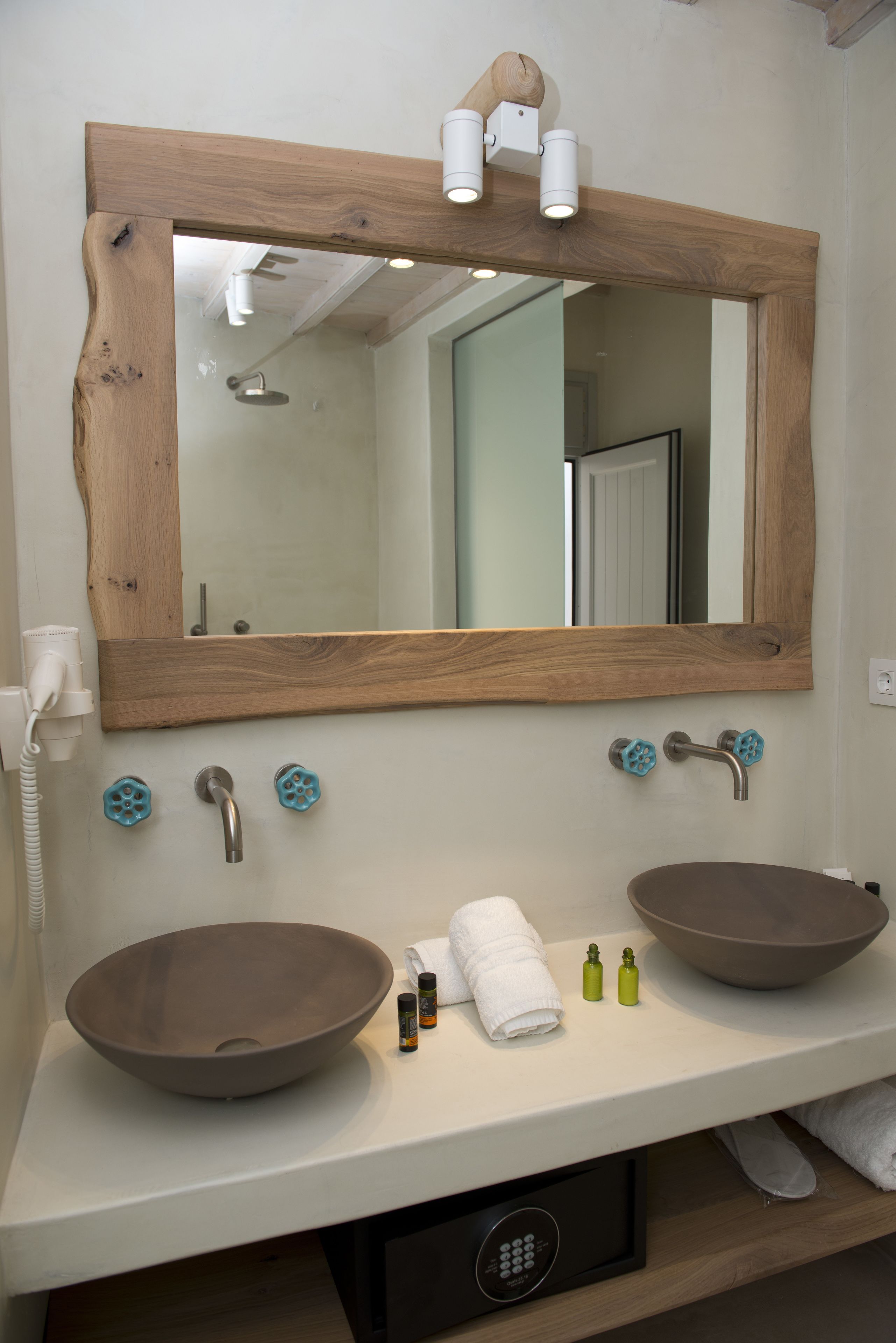 A bathroom with a wooden-framed mirror, two vessel sinks, a towel, and a hairdryer.