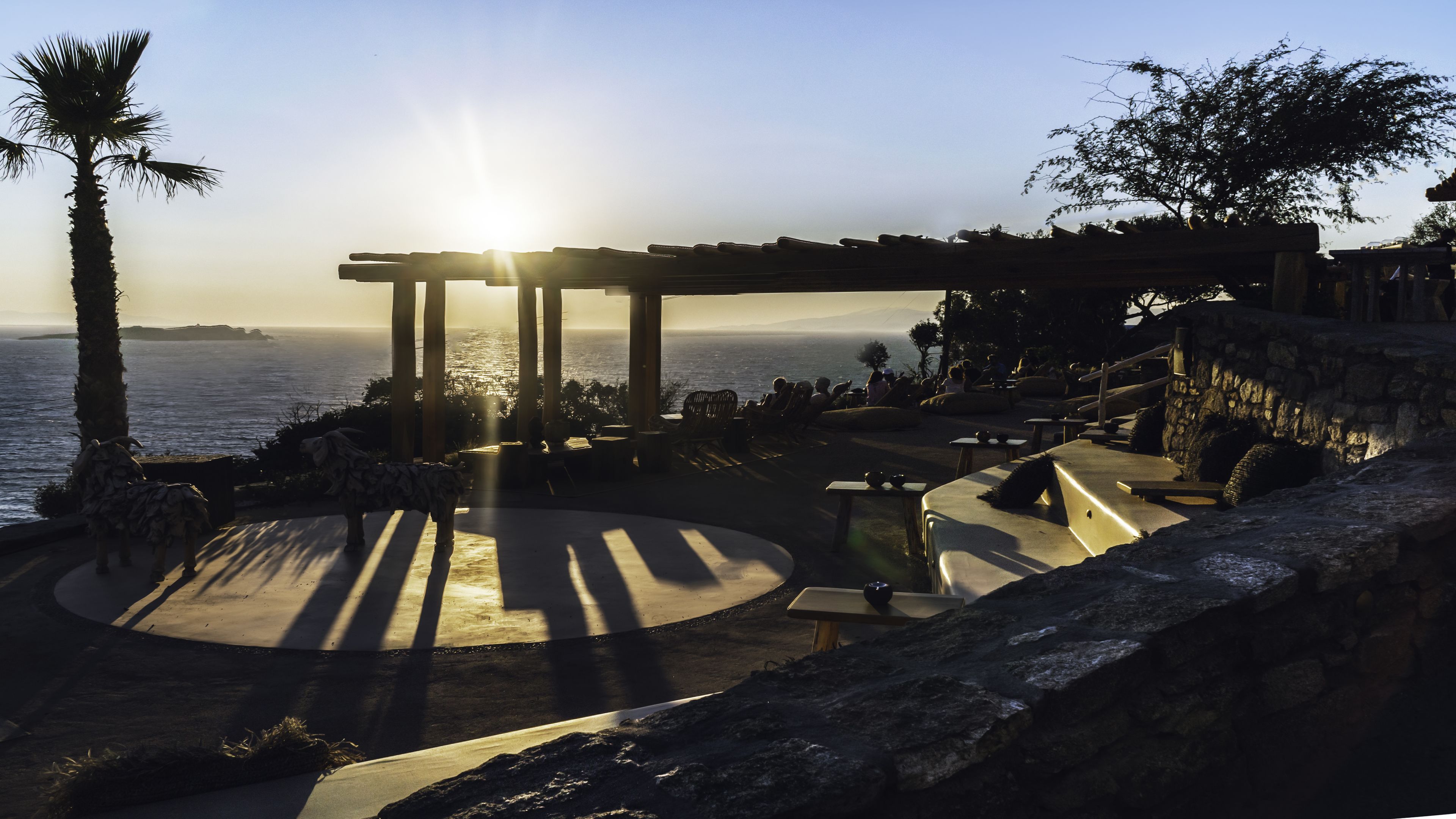 Un espacio al aire libre junto a la costa con vistas al océano, estructuras de piedra y una pérgola.