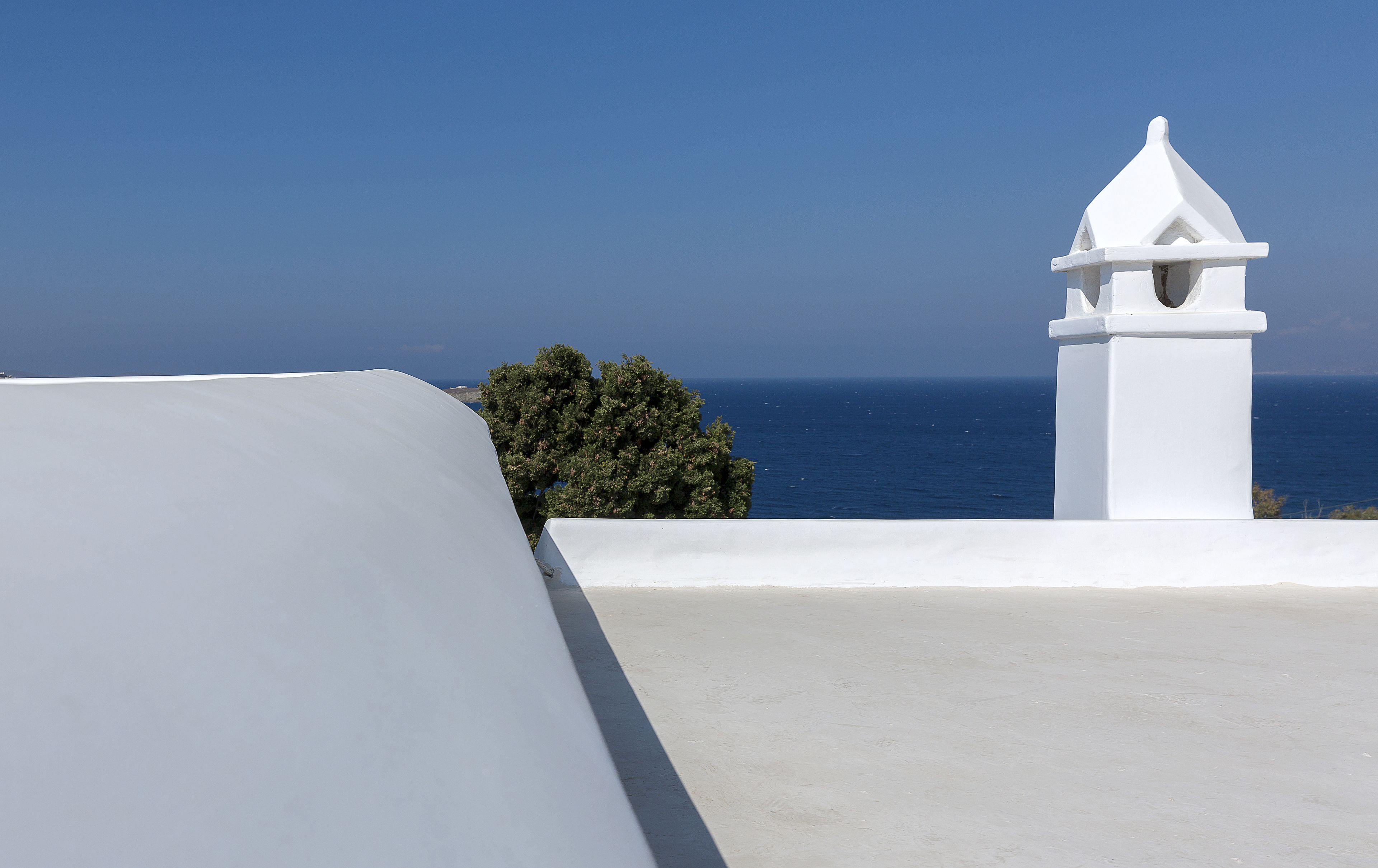 A white building with a small tower, a clear blue sky, and the sea in the background.
