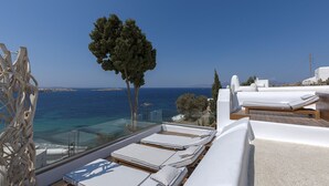 A rooftop terrace with sun loungers and a glass balustrade overlooking the sea.