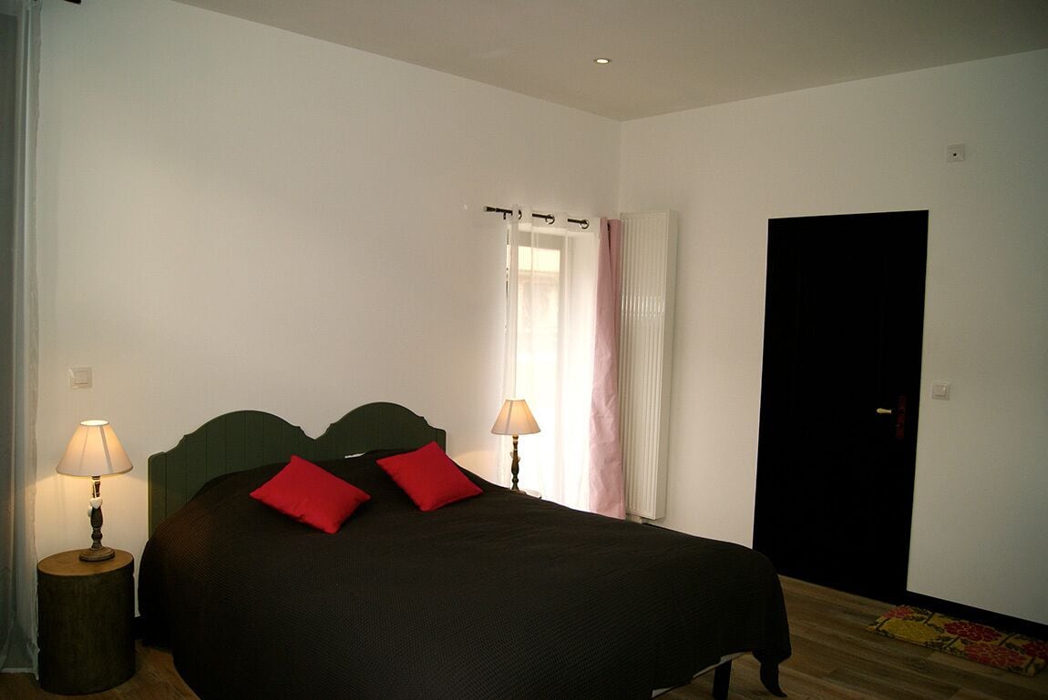 Un dormitorio con cama, dos lámparas de noche, una ventana con cortinas y una puerta.