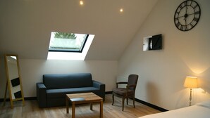 A modern room with a skylight, a sofa, a chair, a small table, a bed, and a wall clock. - La Grange de Salomé (Salomé)