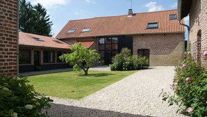 A brick building with a tiled roof, a gravel driveway, and a small lawn area with a tree and bushes. - La Grange de Salomé (Salomé)