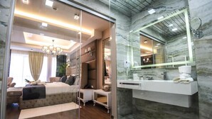 Une chambre à coucher moderne avec un grand lit, une cloison en verre, une coiffeuse avec un miroir et des murs en marbre.