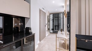 Une chambre d’hôtel moderne dotée d’une paroi en verre, d’une machine à café, d’un bureau et d’une armoire.