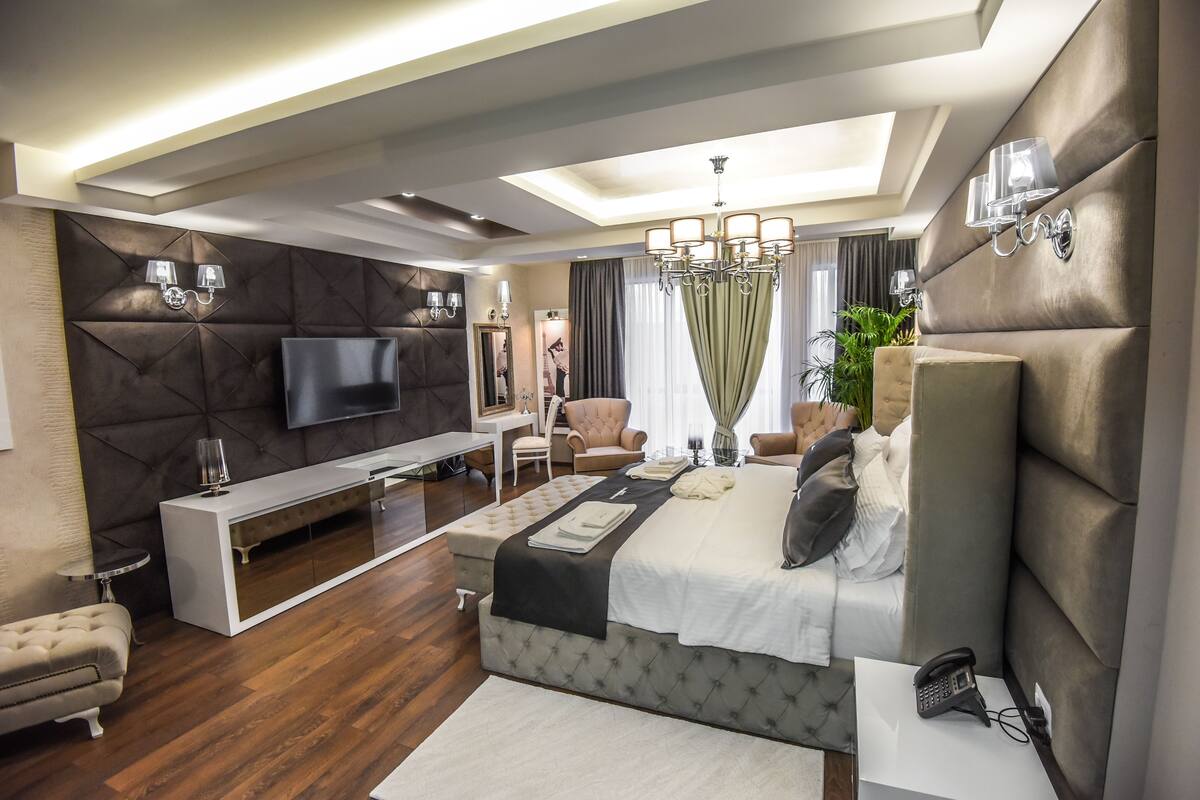 A modern bedroom with a large bed, a TV, a desk, and a seating area.