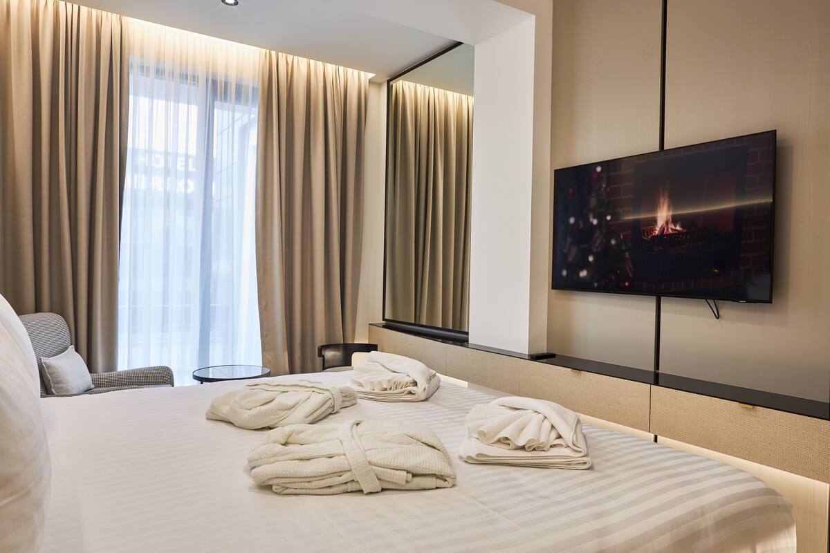 A hotel room with a large bed, a TV mounted on the wall, and a fireplace.