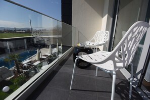 A balcony with two white chairs, a small table with a cup and saucer, and a view of a swimming pool and landscape. - Hotel Mirror Skopje (Petrovec)