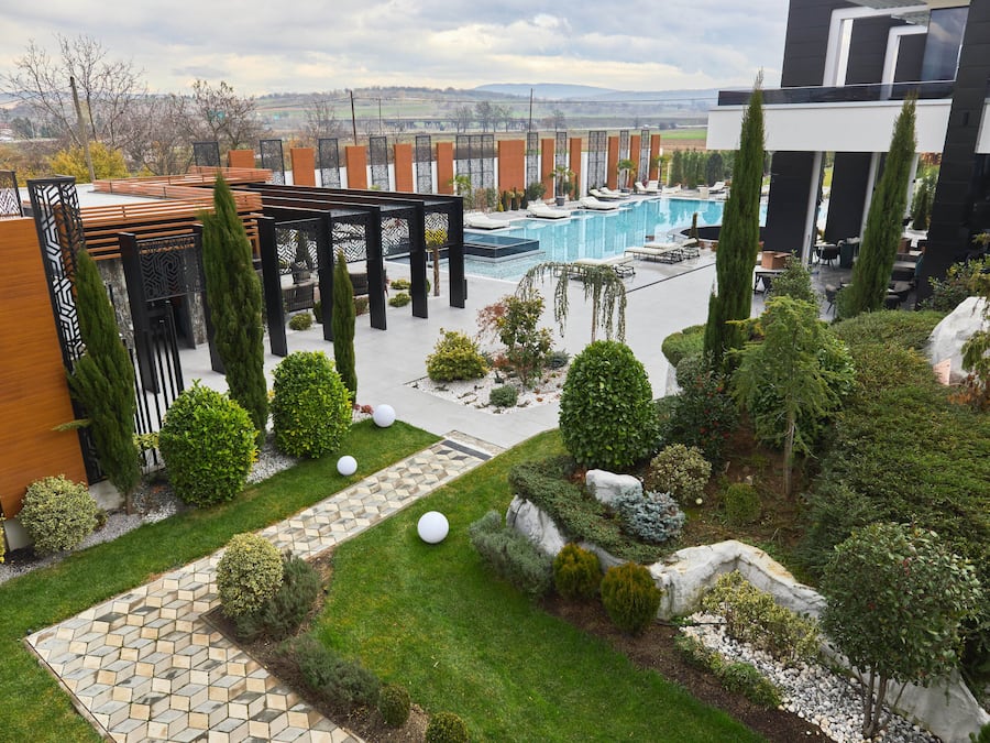 A modern outdoor pool area with a pergola, seating, and a view of the landscape.