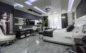 A modern hotel room with a large bed, a desk, a vanity with a mirror, a flat-screen TV, and a large window with curtains. - Hotel Mirror Skopje (Petrovec)
