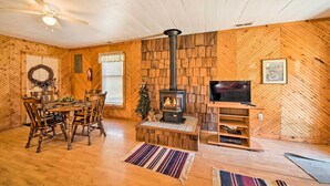 Un salon chaleureux avec un mur en bois à motifs en chevrons, une cheminée, une table à manger avec des chaises, un téléviseur et un ventilateur de plafond.