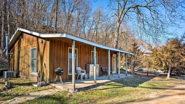 Une cabane en bois avec un porche couvert, un barbecue et une chaise à l’extérieur.