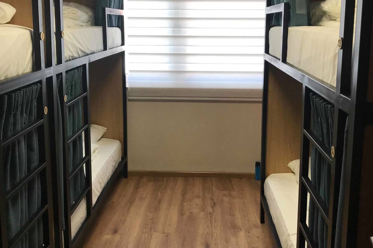 Una habitación con literas, suelo de madera y una ventana con persianas.